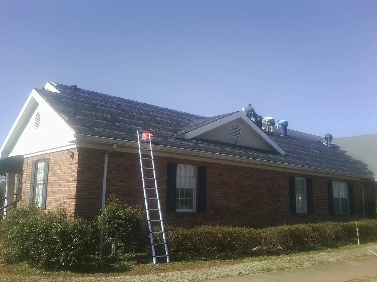 Crew tearing shingles off a brick ranch roof with a ladder set — Emergency Roof Repair work by our crew in Loudonville