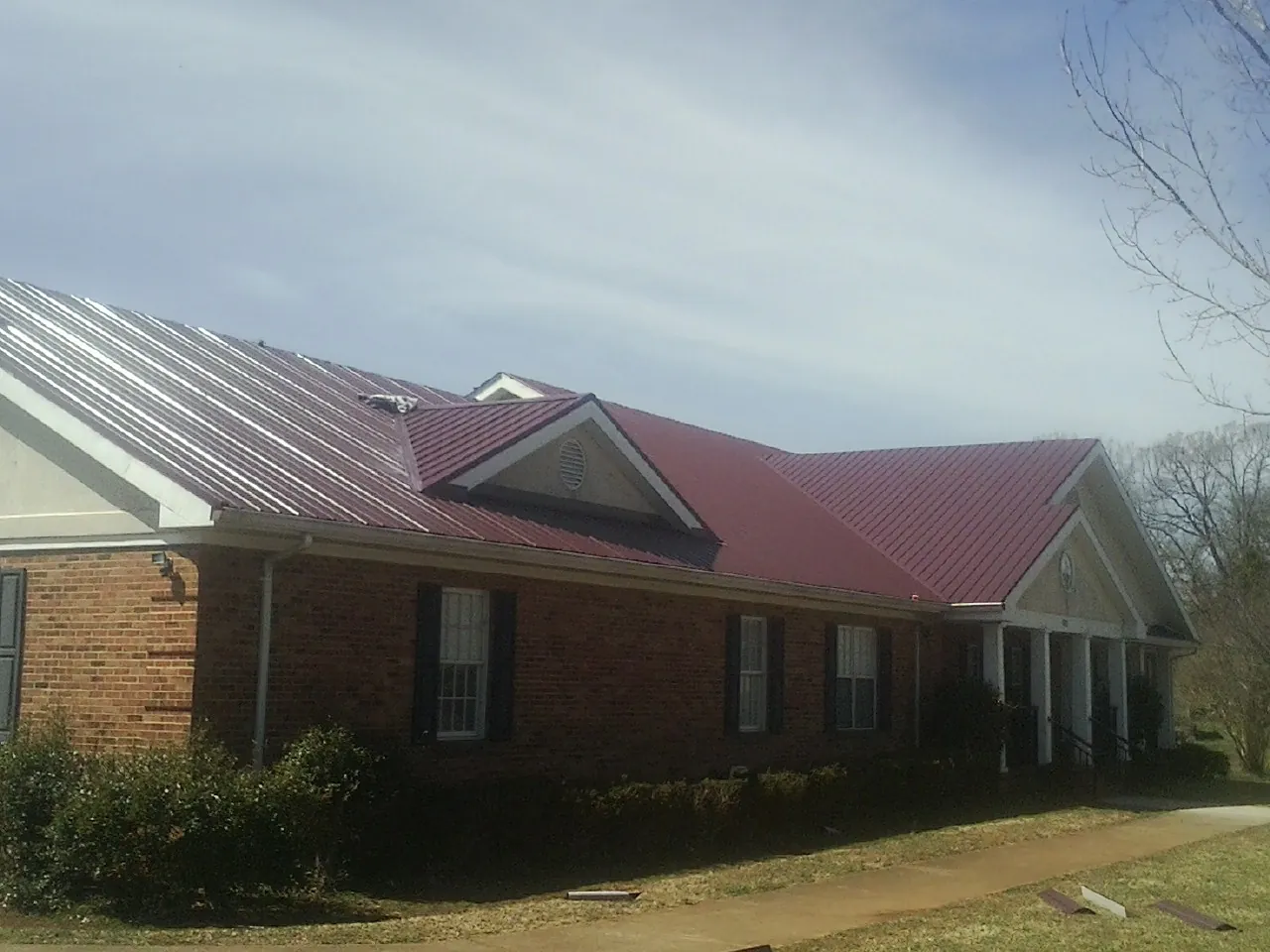 Red metal roof with gabled entries on a long brick building, from a Hail Damage Roof Repair job in Loudonville