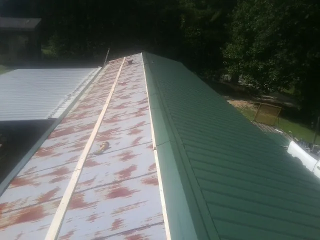 Old rusted panels beside newly installed green metal roofing — Wind Damage Roof Repair by Roofing Brothers in Loudonville