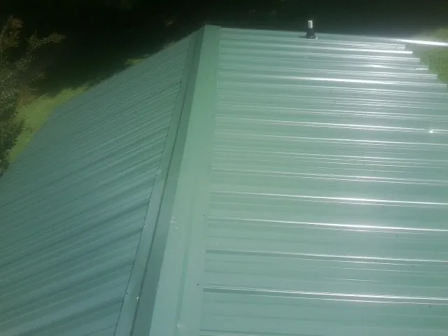 New green metal panels meeting at the ridge of a roof — Flat Roof Repair work by our crew in Loudonville
