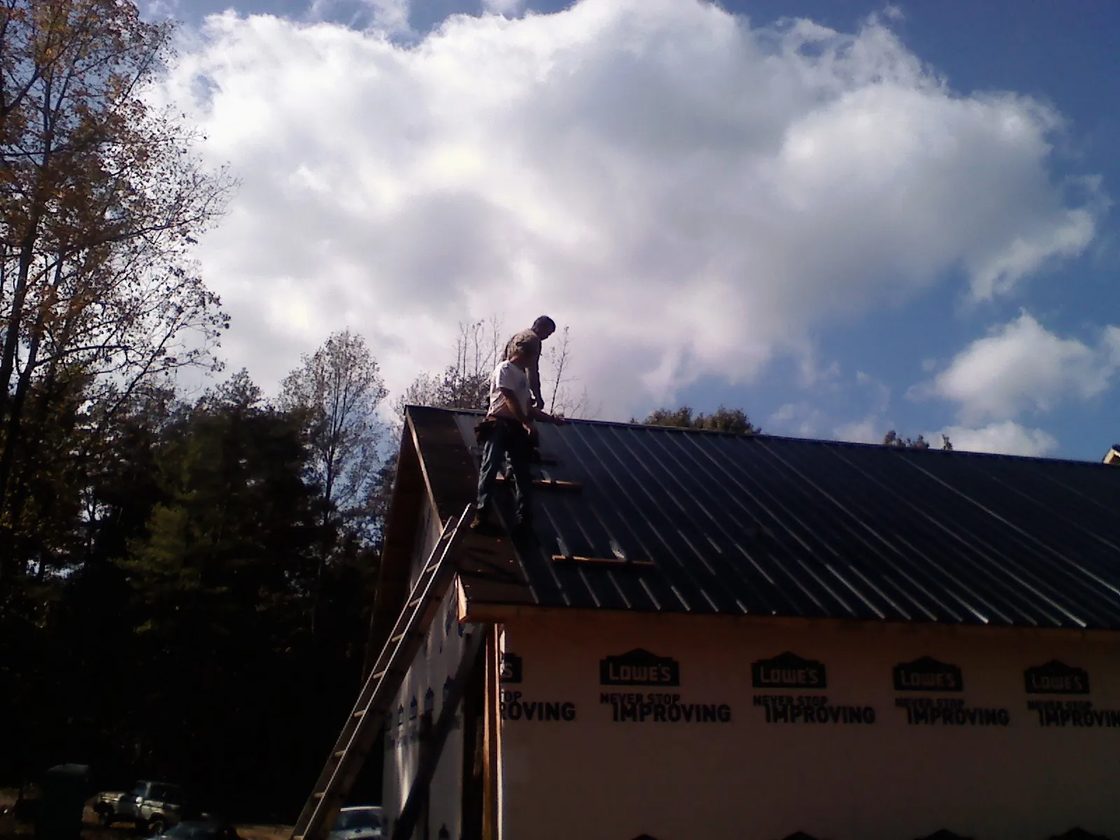 Roofer fastening dark metal panels high against a cloudy sky, from a Roof Inspection job in Loudonville