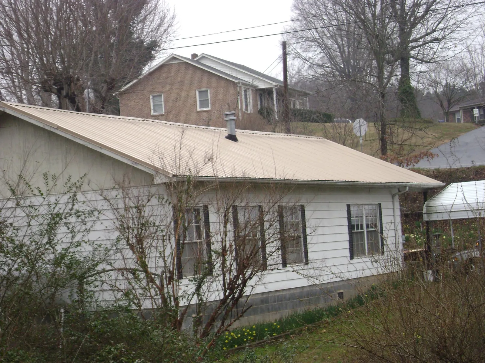 Tan metal roof on a white sided house set into a hillside — Commercial Roofing by Roofing Brothers in Loudonville
