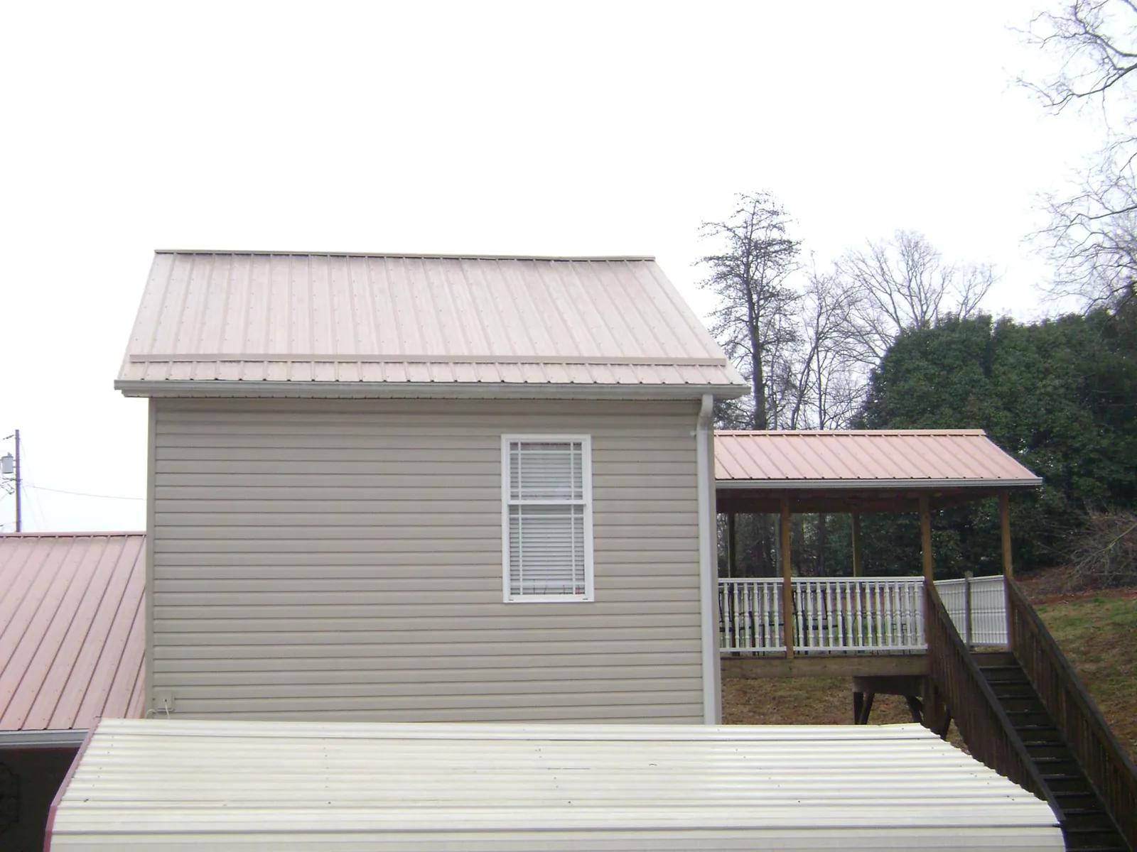 Tan metal roofs on a two story addition and attached porch, from a Roof Replacement job in Loudonville